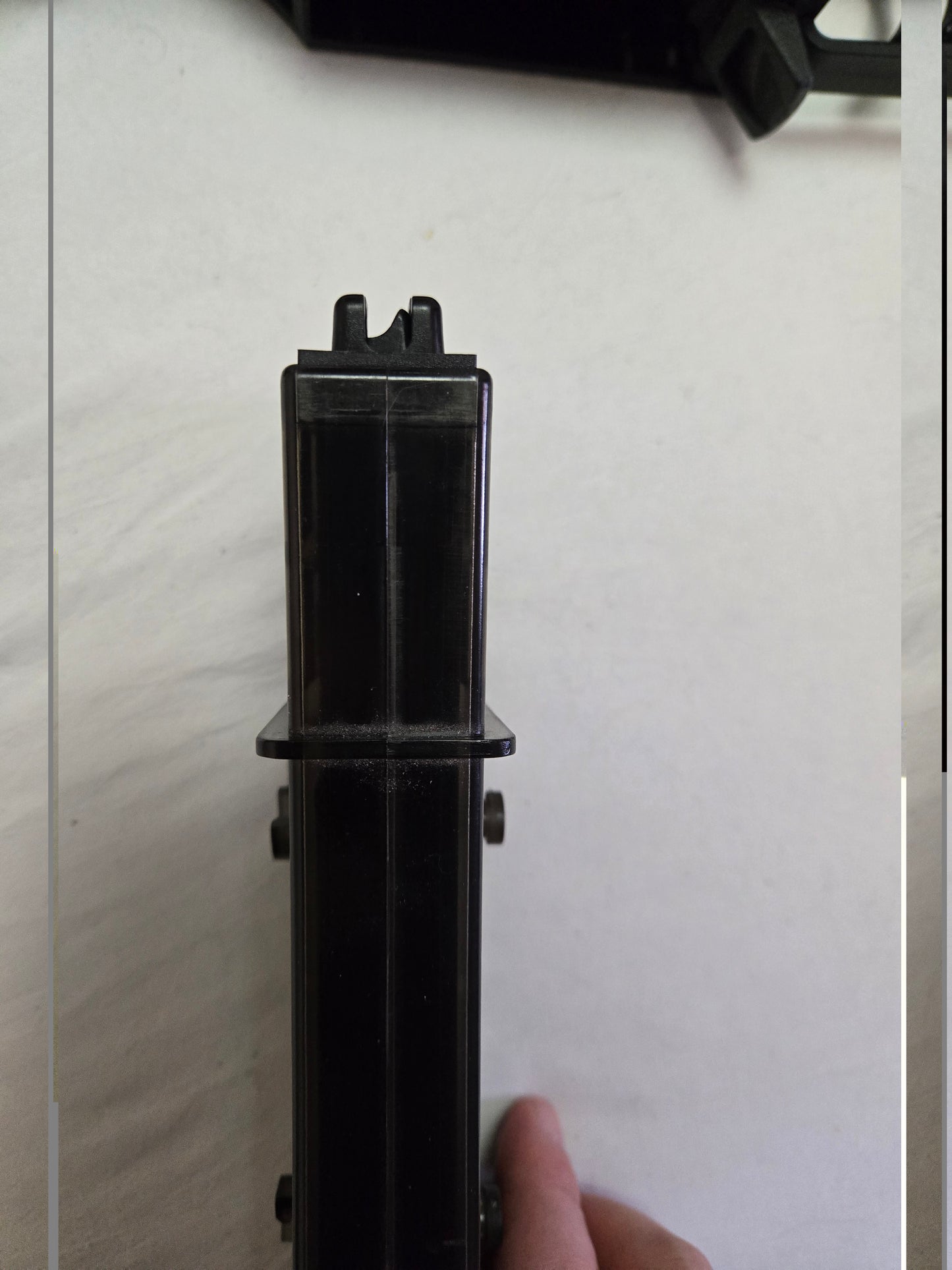 Black metal rod or pipe on a light gray surface with a hand partially visible.